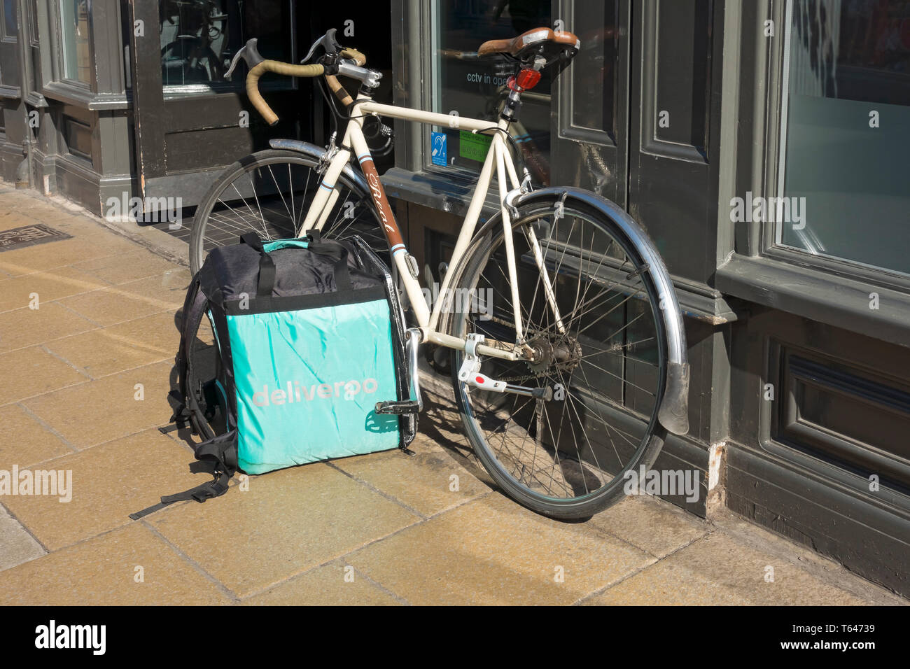 Close up of Deliveroo box food meal delivery company service and bike parked outside restaurant England UK United Kingdom GB Great Britain Stock Photo