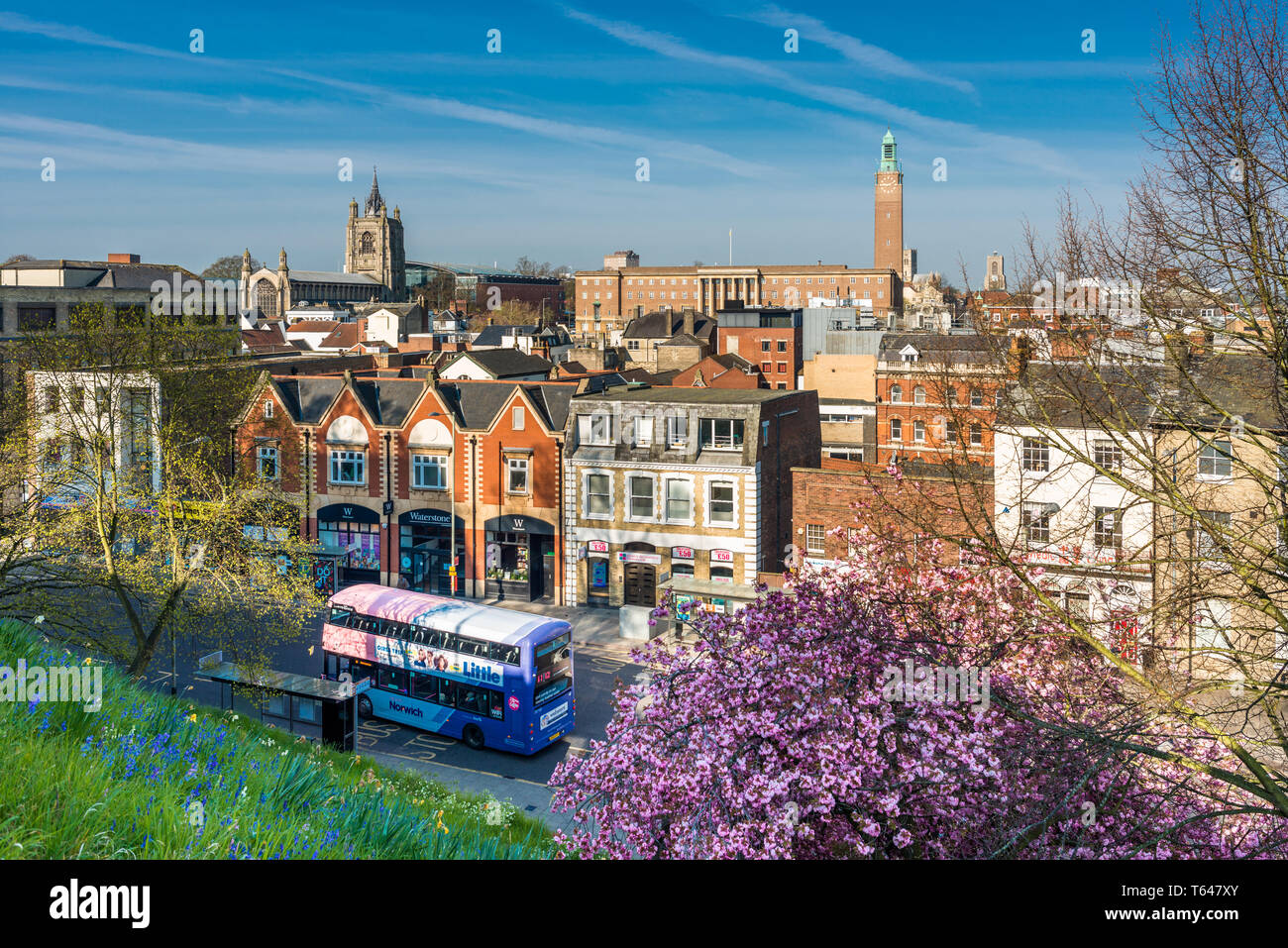 Norwich city skyline with spires of St. Peter Mancroft church and City hall tower and tourist bus passing by, viewed from Castle hill. Norfolk, UK. Stock Photo