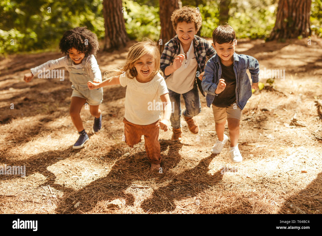 Group of kids running up in the forest. Multi-ethnic children playing together in forest. Stock Photo