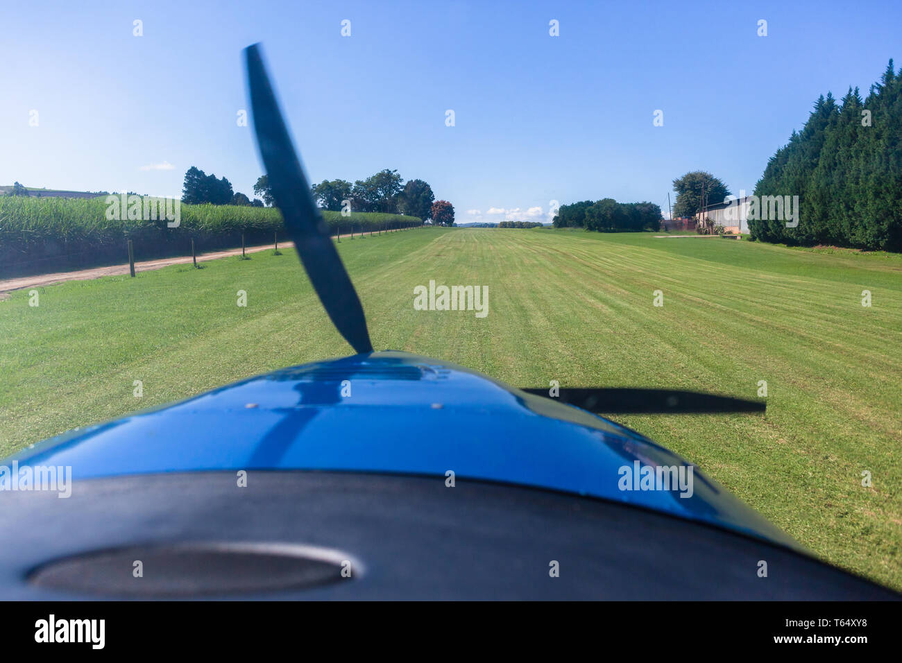 Pilots cockpit takeoff flight view in light propeller aircraft plane in rural farming countryside grass runway. Stock Photo