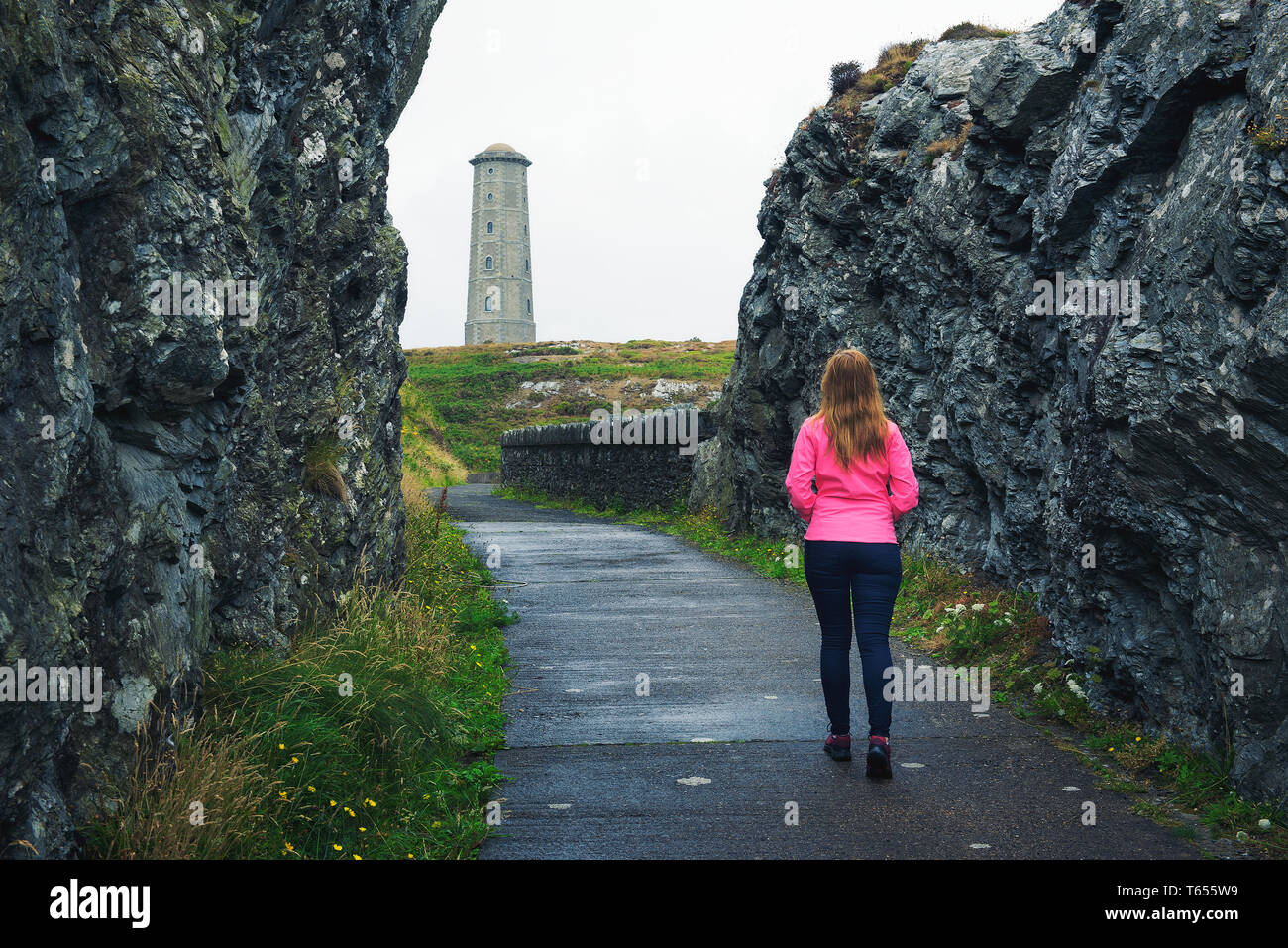 Young woman walking towards Wicklow Head Lighthouse in Ireland Stock Photo