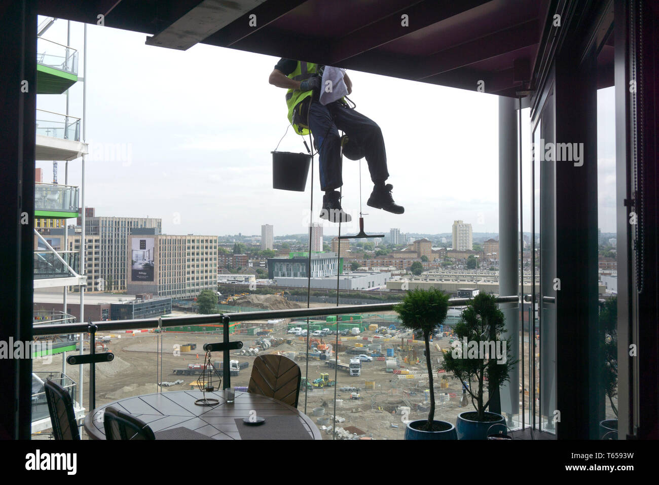 A window cleaner dangles from a balcony by ground work construction by US property investor Greystar for £101m in London. 22/08/2017 Stock Photo