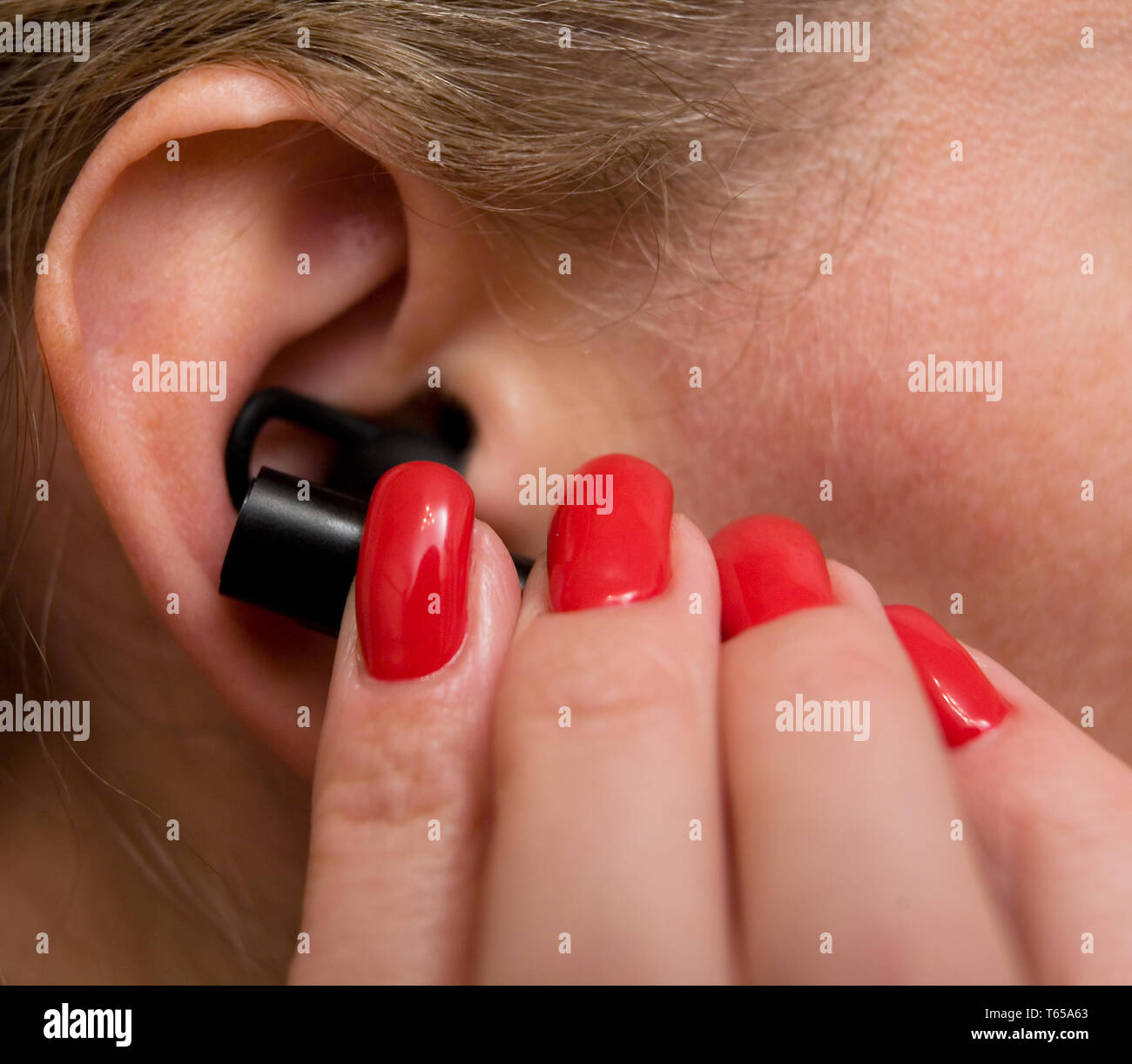 Beautiful well-groomed female fingers insert a headset into your ear. Close-up. Stock Photo