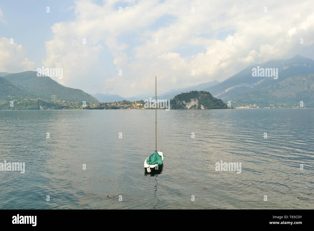 Beautiful panoramic view to Bellagio peninsula and lake Como with a sailing boat anchored in water from Varenna lakefront in a spring sunny day. Stock Photo