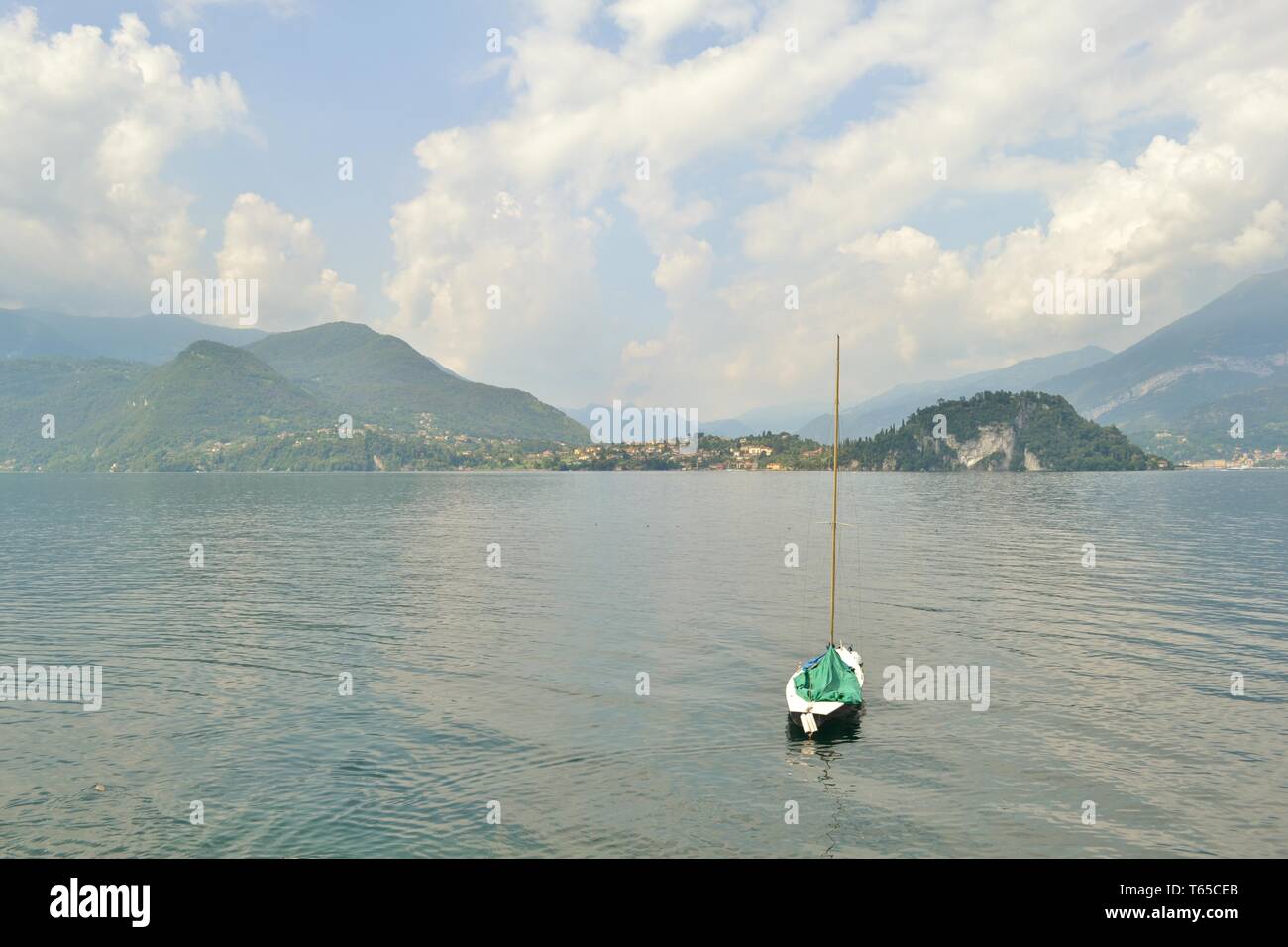 Beautiful panoramic view to Bellagio peninsula and lake Como with a sailing boat anchored in water, from Varenna lakefront in a spring sunny day. Stock Photo