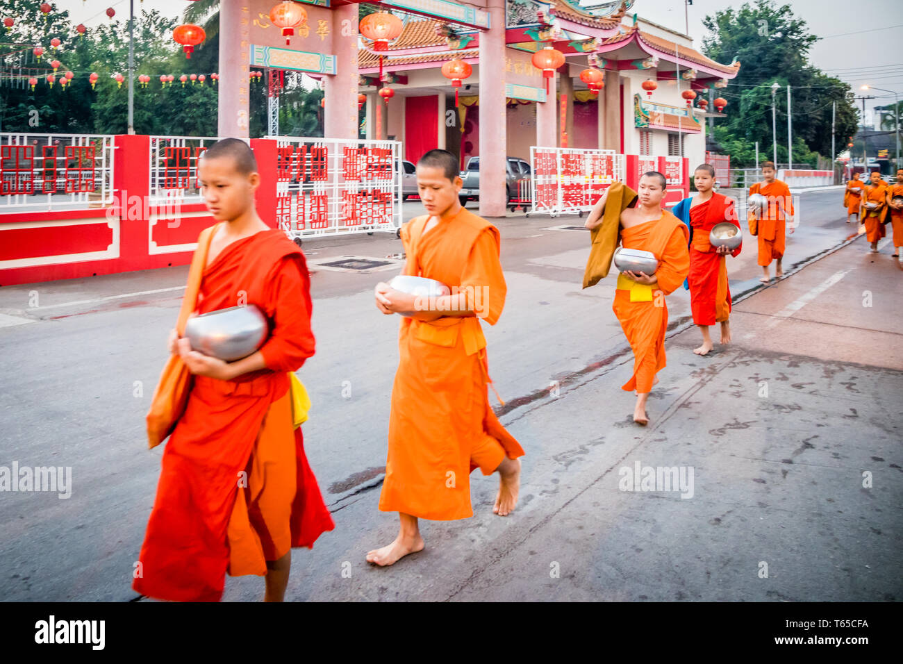 Mae Sot, Thailand - 3rd February 2019:   Young monks walking in a line past Chinese temple. Monks collect alms every morning. Stock Photo