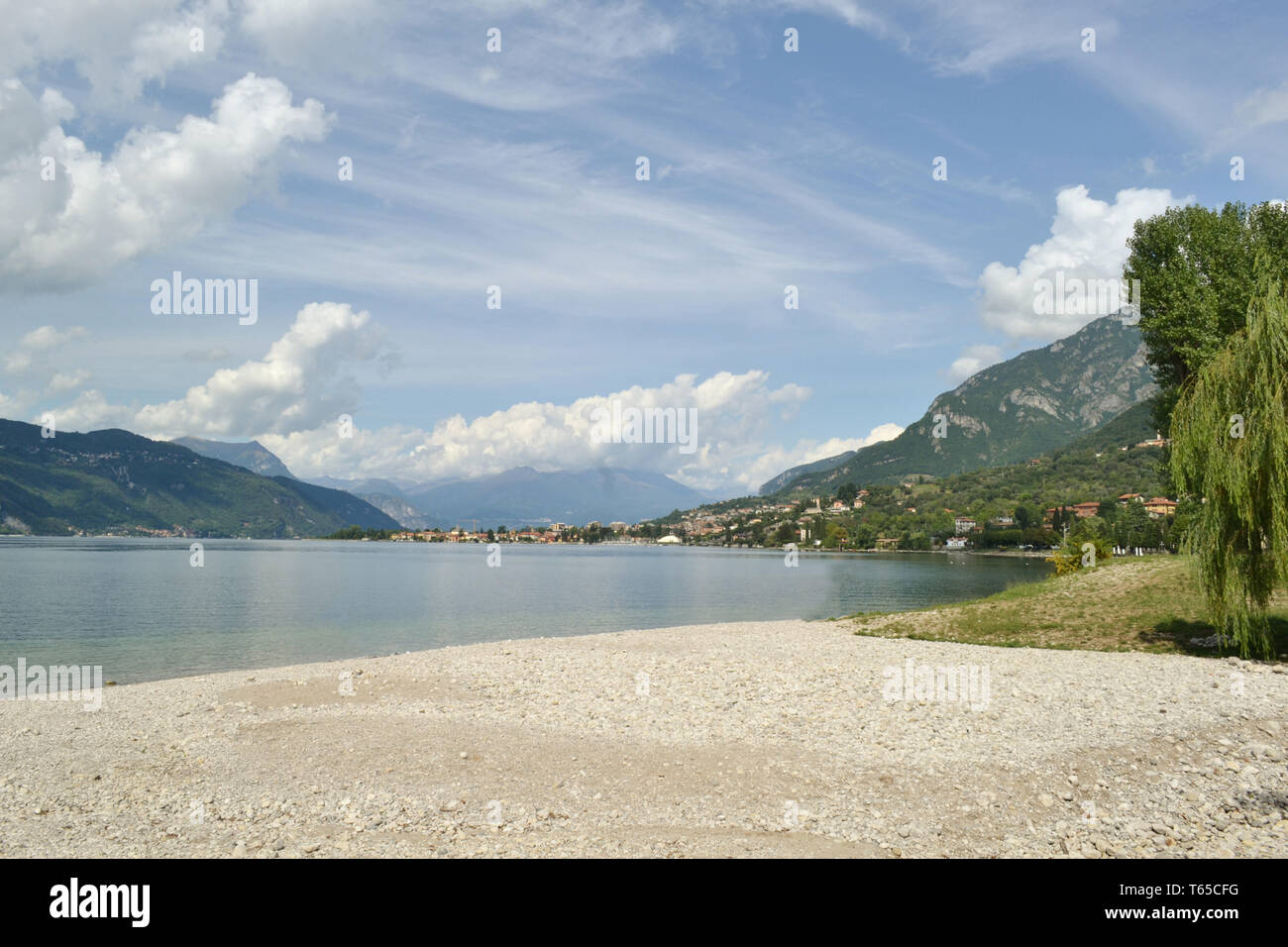 Beautiful summer panoramic view from the pebble beach of Abbadia Lariana to the lake Como and Mandello del Lario town in a sunny hot day. Stock Photo