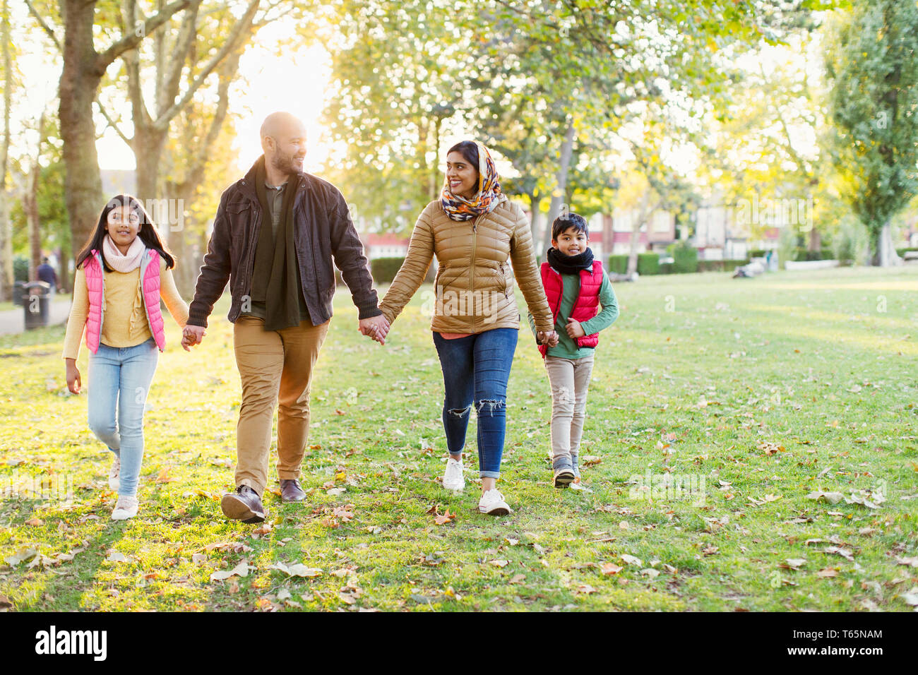 Muslim family holding hands, walking in sunny autumn park Stock Photo