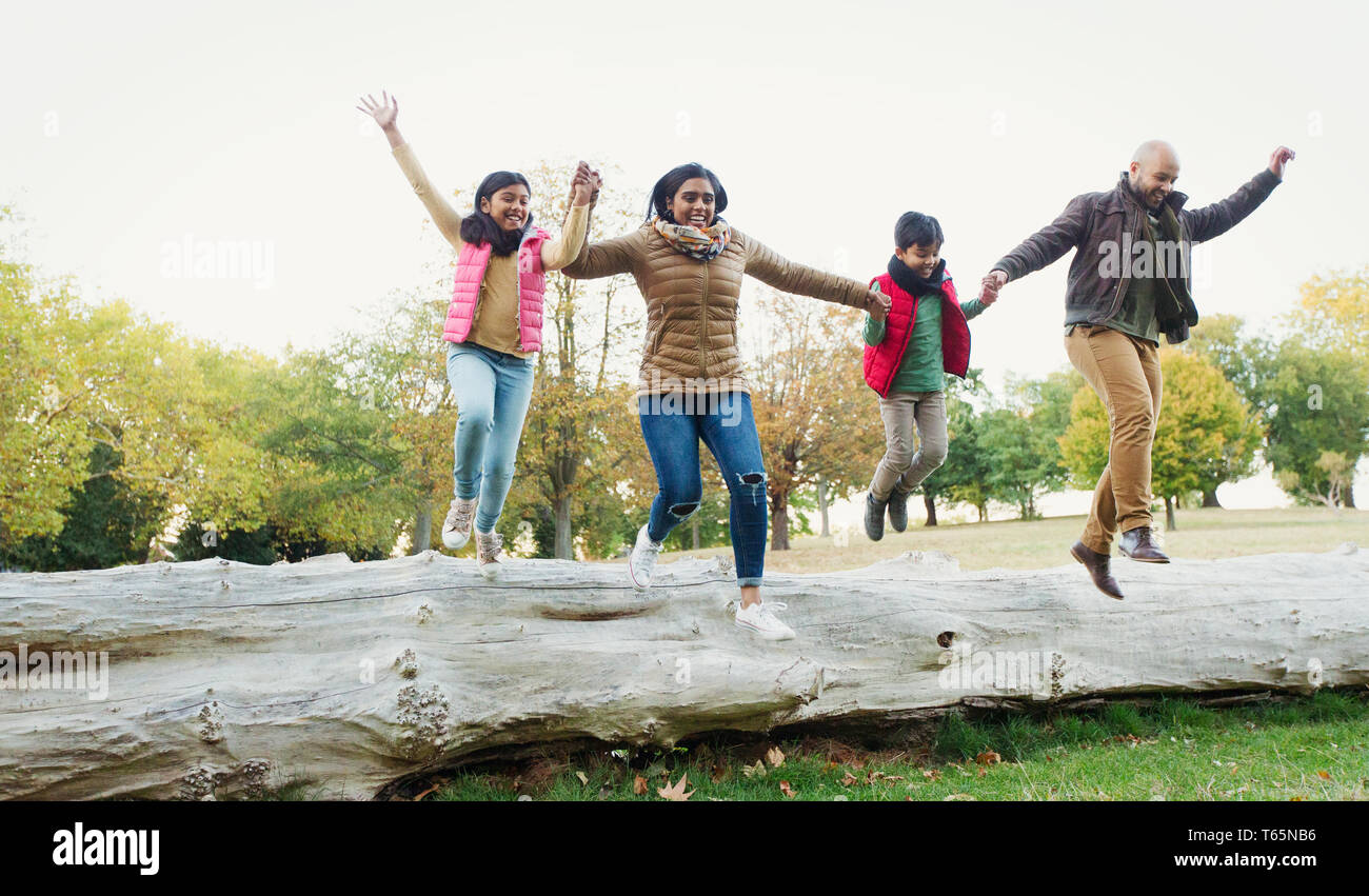 Happy, playful family holding hands, jumping off log in autumn park Stock Photo