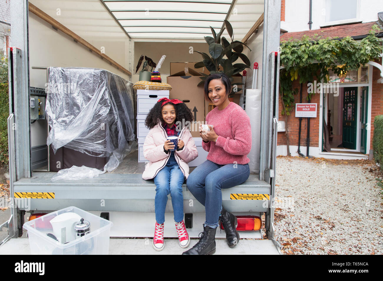 Portrait happy mother and daughter drinking tea at back of moving van, moving house Stock Photo