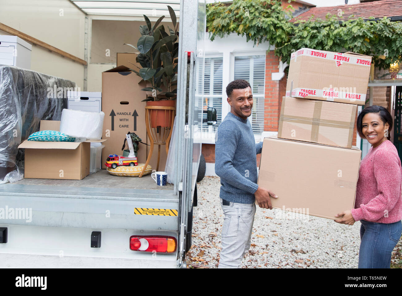 Portrait happy couple moving house, unloading cardboard boxes from moving van Stock Photo