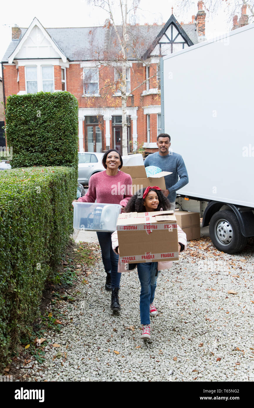 Family moving into new house, carrying  belongings from moving van in driveway Stock Photo