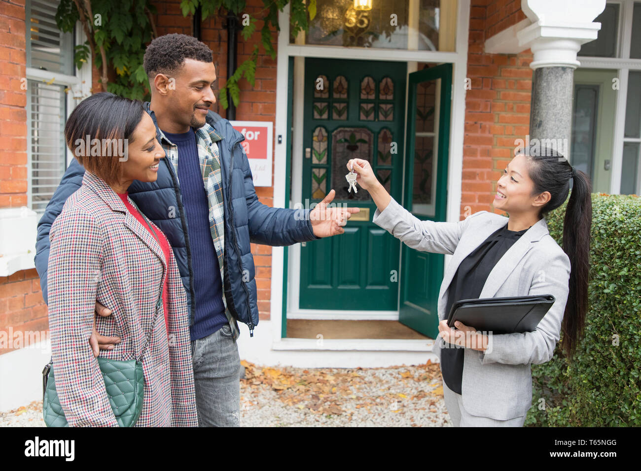 Real estate agent giving house keys to couple outside new house Stock Photo