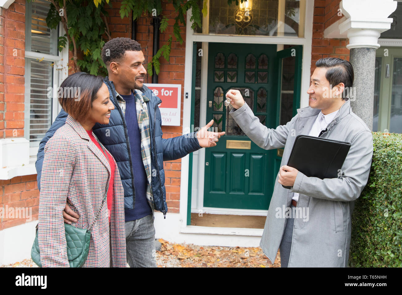 Real estate agent giving house keys to couple outside house for sale Stock Photo