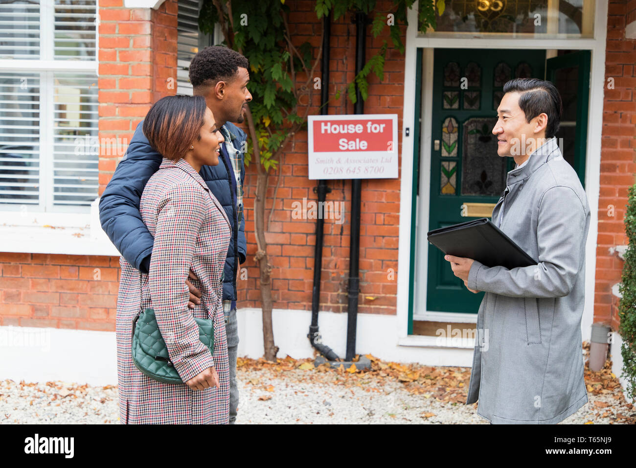 Real estate agent talking with couple outside house for sale Stock Photo