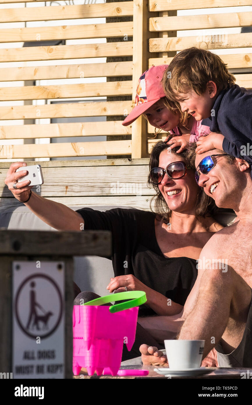 A happy family of holidaymakers taking a selfie with an iPhone at a sunny Fistral in Newquay in Cornwall. Stock Photo