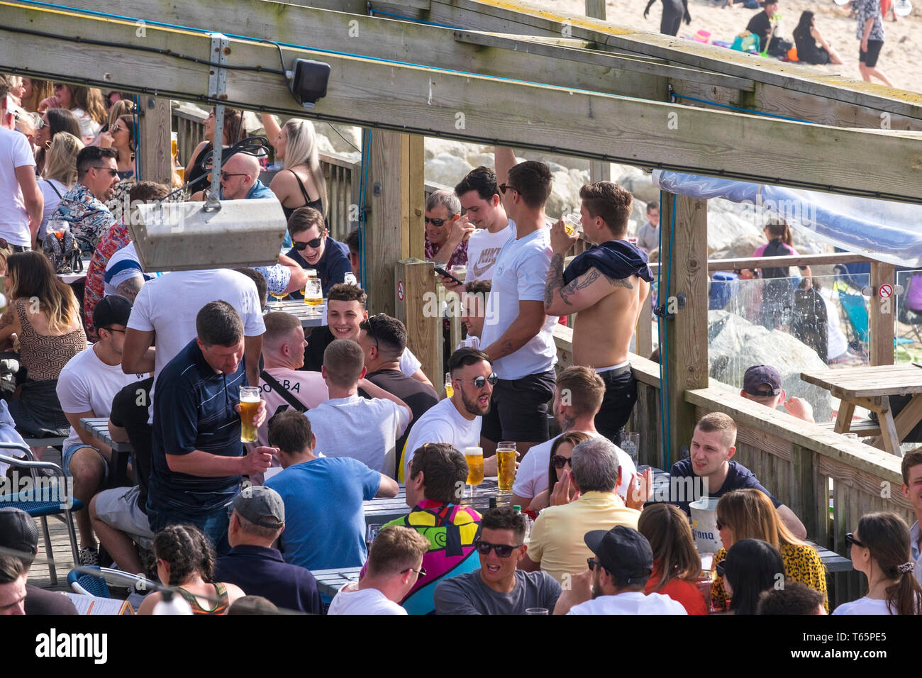 People drinking and socialising socializing on the outdoor deck area of the Fistral Beach Bar in Newquay in Cornwall. Stock Photo
