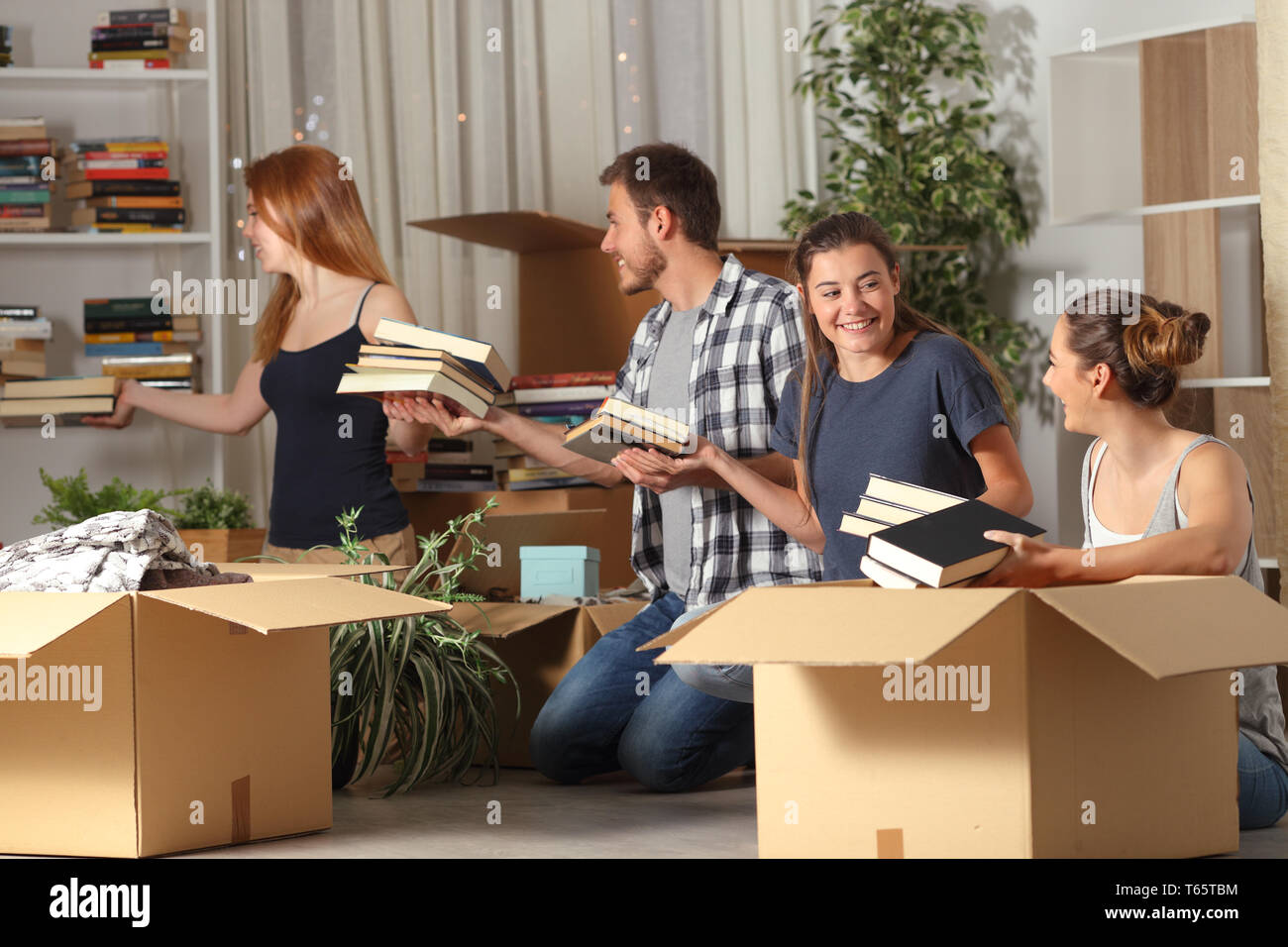 Four happy roommates cooperating boxing belingings moving home in the night Stock Photo