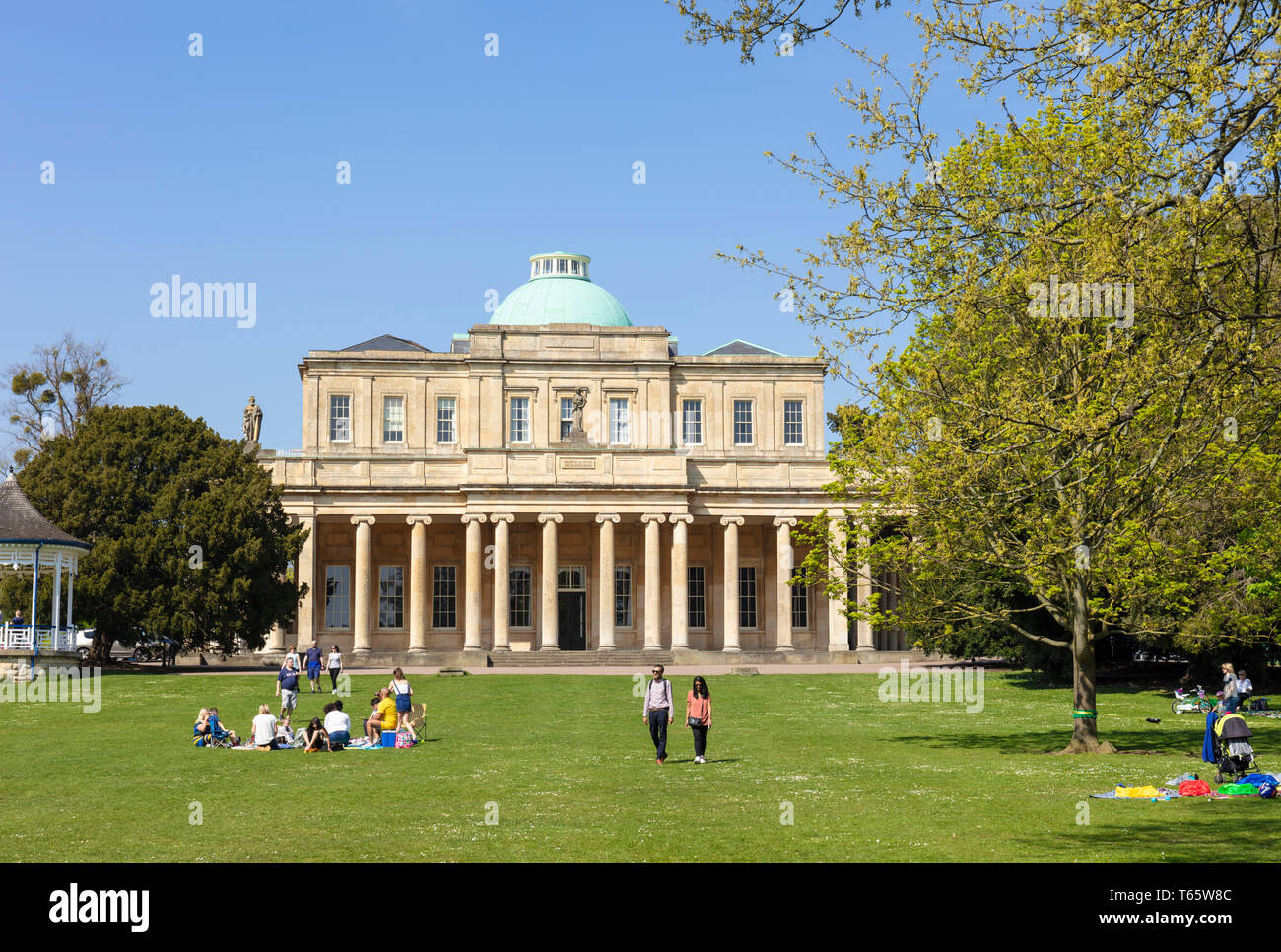 Cheltenham Pittville Pump Room with people having a picnic and children playing Pittville Park, Cheltenham Spa Gloucestershire, England, UK,GB, Europe Stock Photo