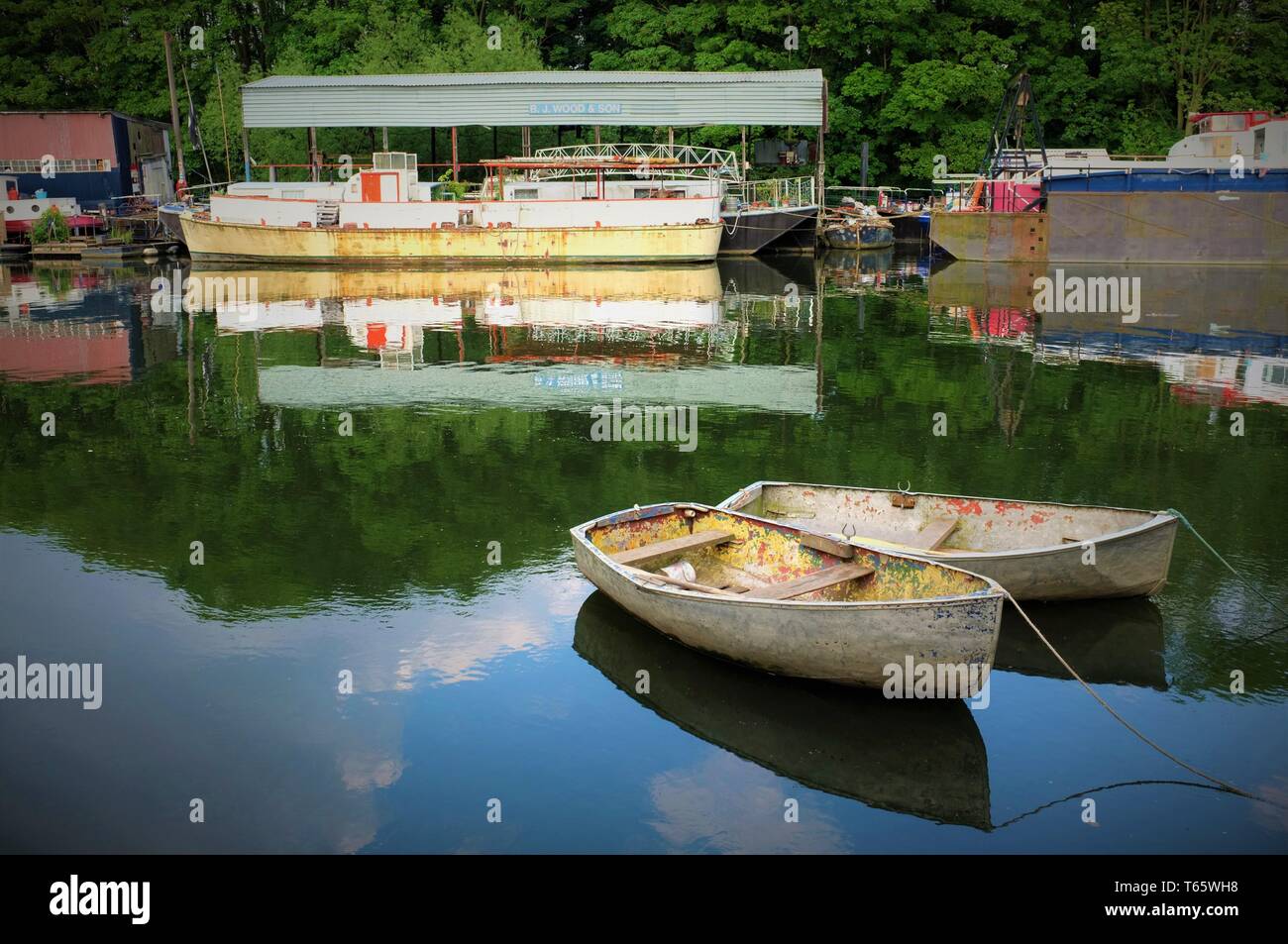 Two rowing boats moored on water in River Thames at Isleworth, with boatyard beyond (version 2) Stock Photo