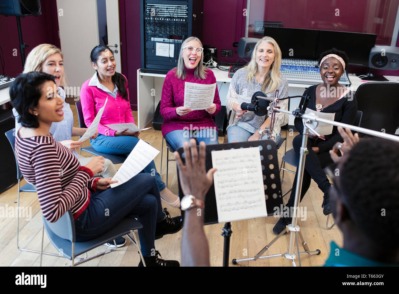 Male conductor leading womens choir with sheet music singing in music recording studio Stock Photo
