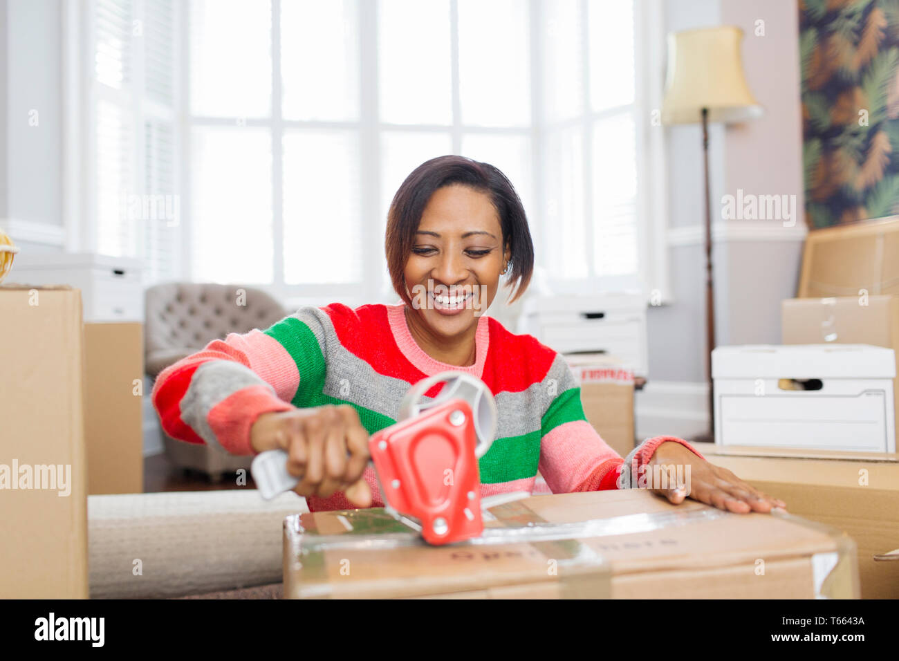 Smiling woman taping moving boxes, moving house Stock Photo