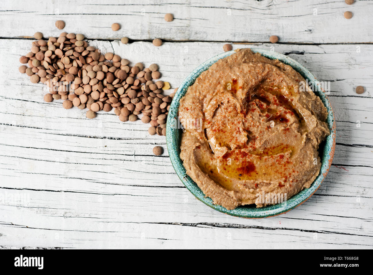 high angle view of a green ceramic plate with a homemade lentil hummus, seasoned with paprika, on a white rustic wooden table Stock Photo