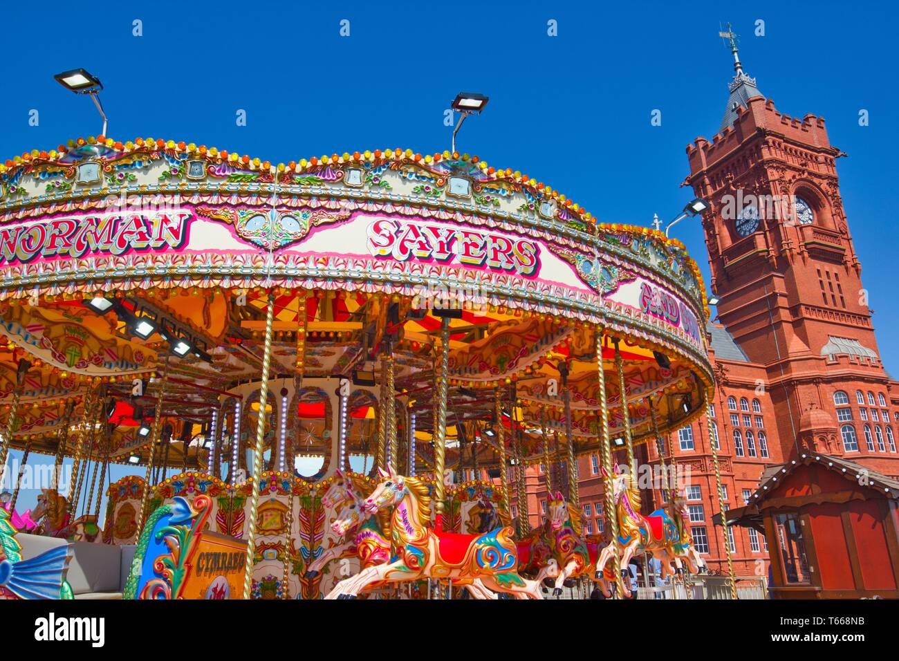 Fairground carousel ride and tower of the Grade 1 Listed Pierhead Building (Adeilad y Pierhead), Cardiff Bay, Wales, United Kingdom. Stock Photo