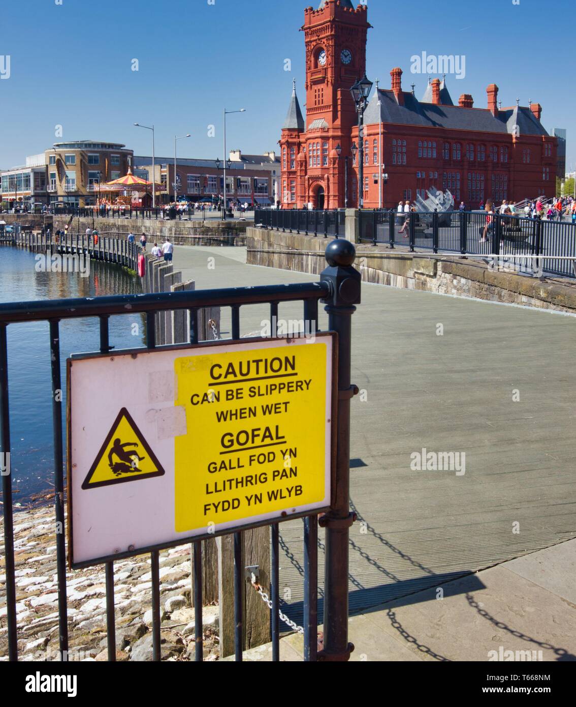 Slippery when wet warning sign in Welsh and English and the pierhead building, Cardiff Bay, Cardiff, Wales, United Kingdom Stock Photo