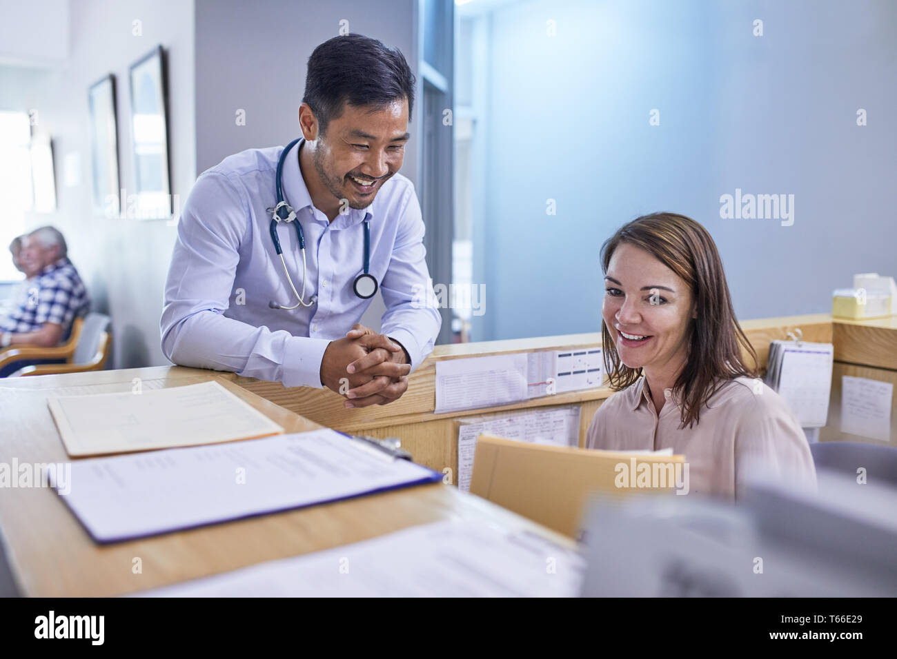 Smiling doctor and receptionist discussing medical record in clinic Stock Photo