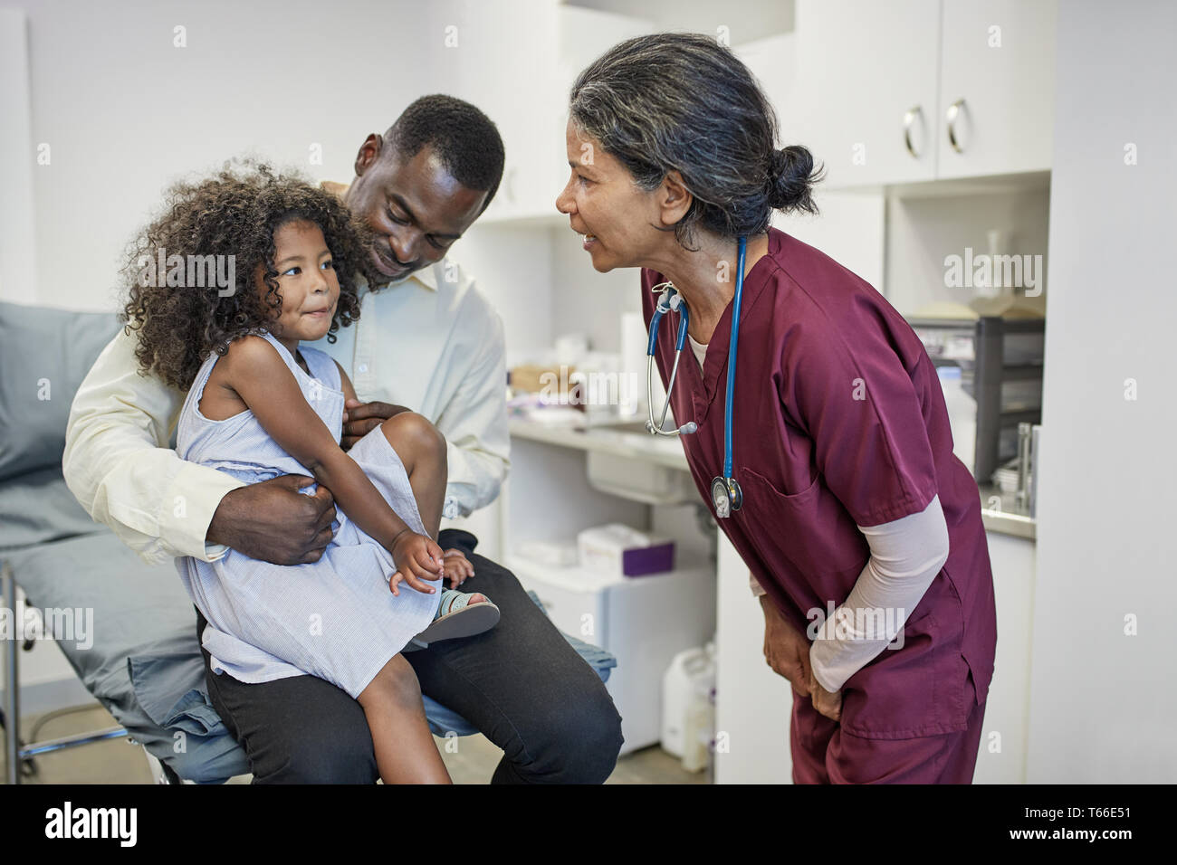 Female pediatrician talking to father and daughter in clinic examination room Stock Photo