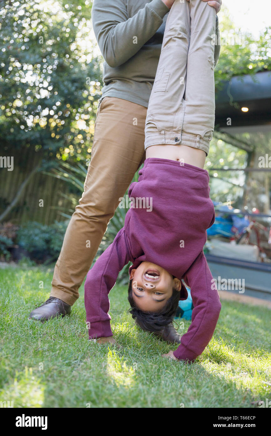 Playful boy hanging upside down in backyard Stock Photo