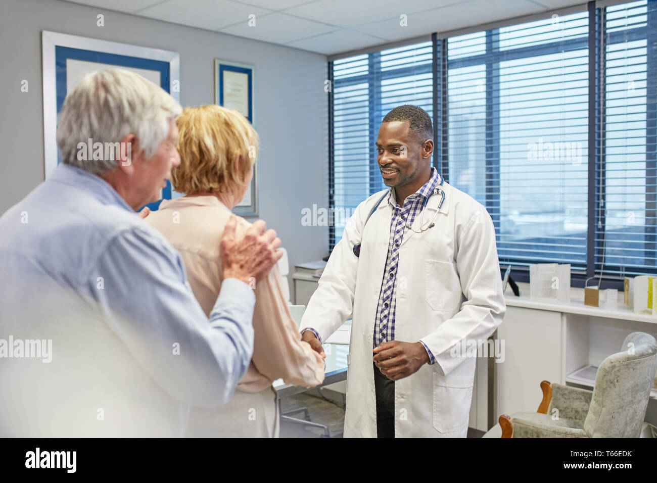 Doctor shaking hands with senior couple in doctors office Stock Photo