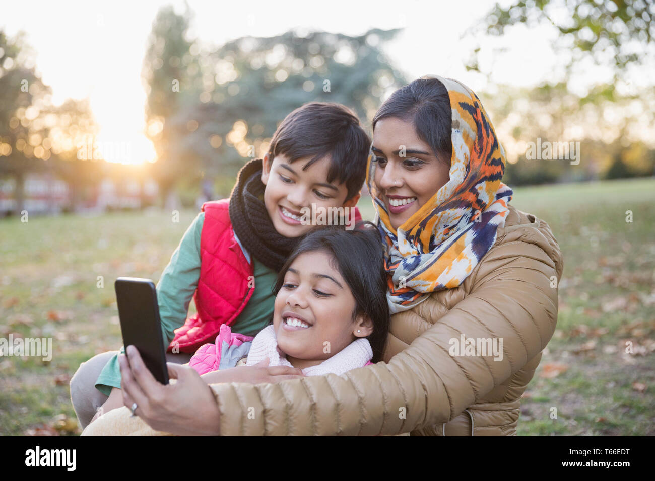 Muslim mother in hijab taking selfie with camera phone in autumn park Stock Photo