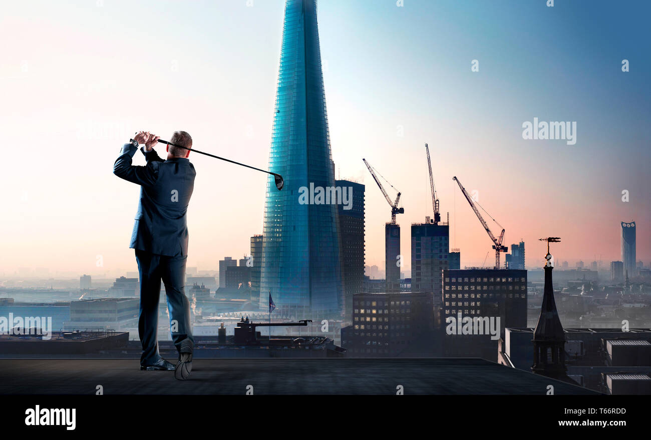 Businessman swinging golf club on city highrise rooftop Stock Photo