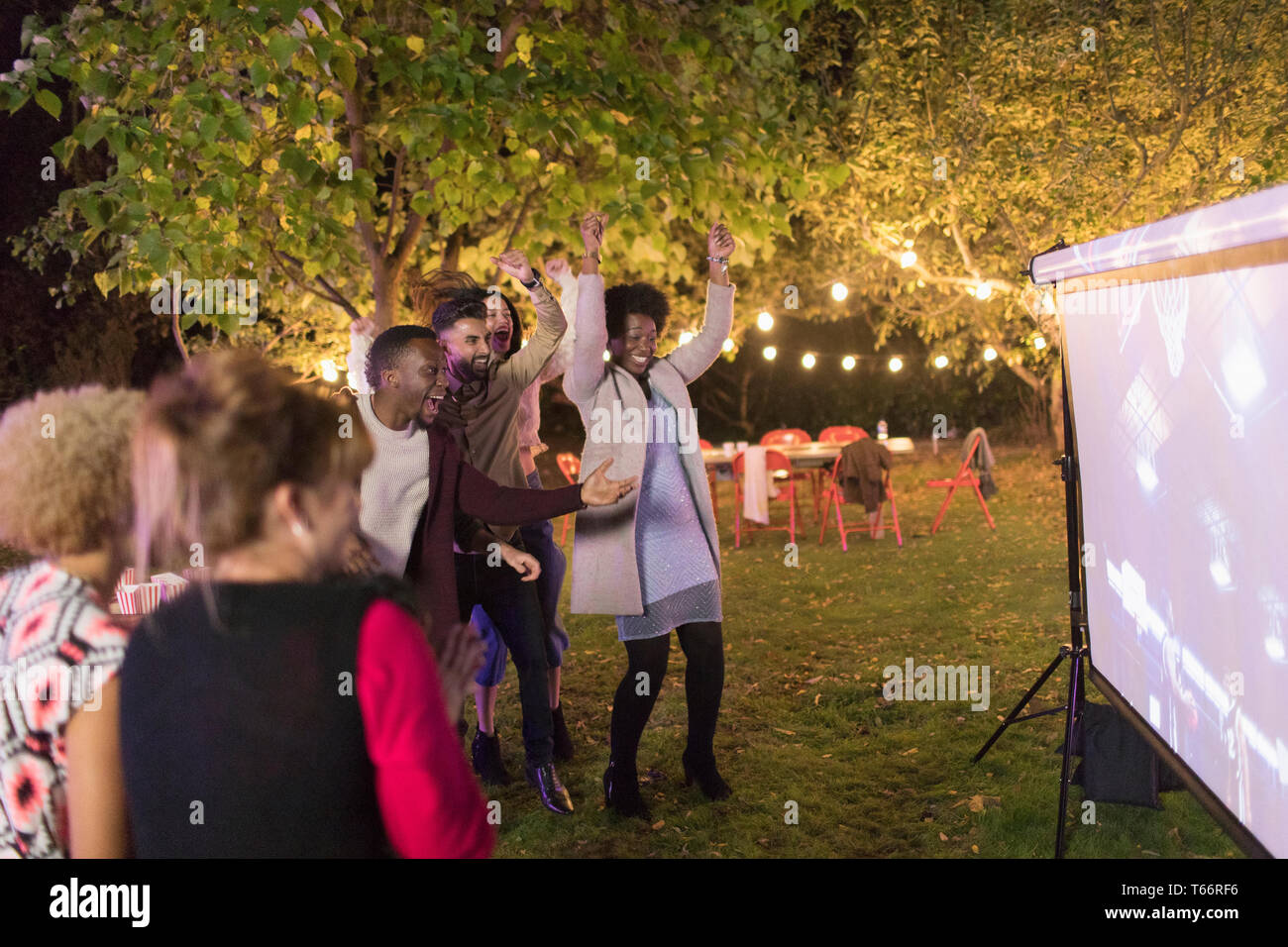 Friends cheering, watching basketball on projection screen in backyard Stock Photo