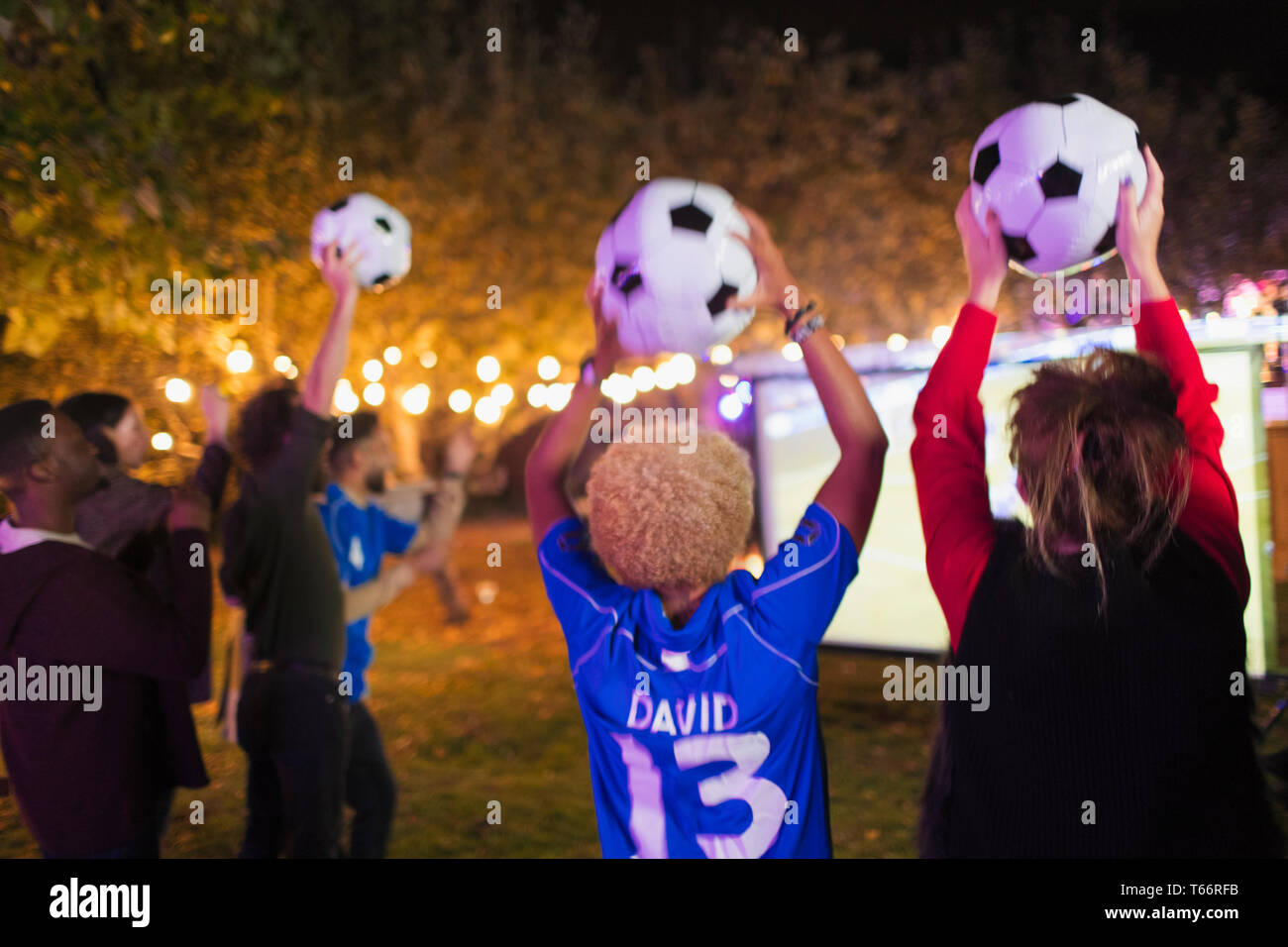 Happy friends with soccer balls cheering, watching soccer match in backyard Stock Photo