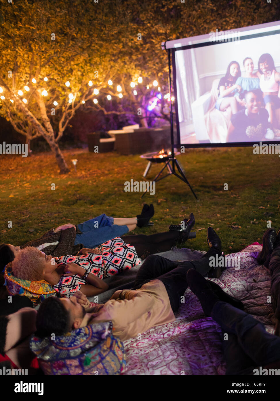 Friends relaxing, watching movie on projection screen in backyard Stock Photo