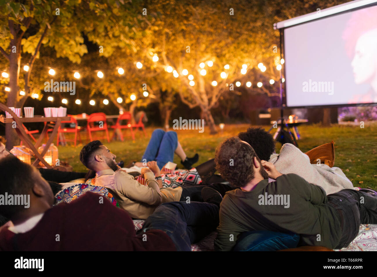 Friends relaxing, watching movie on projection screen in backyard Stock Photo