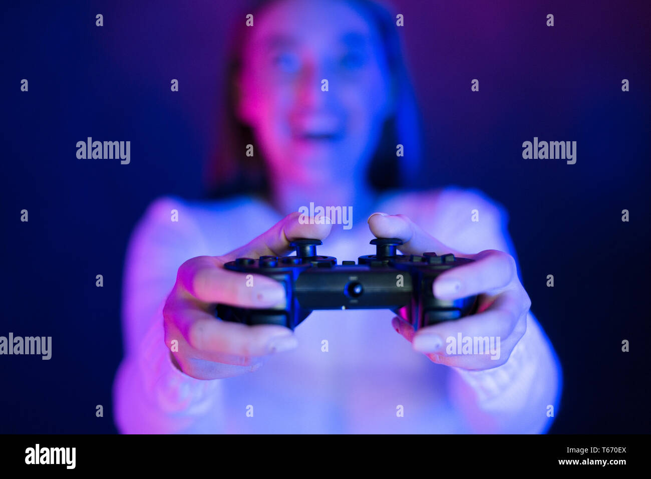 Woman Playing Video Games At Night. Pushing on buttons illuminated with neon lights Stock Photo