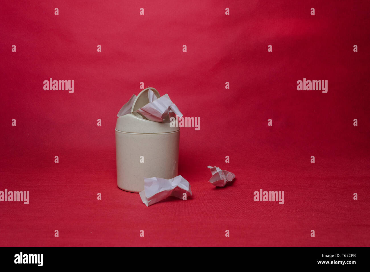 Light trash bin on a red background. Closeup of crumpled sheets of paper. The concept of environmental recycling of paper waste. Stock Photo