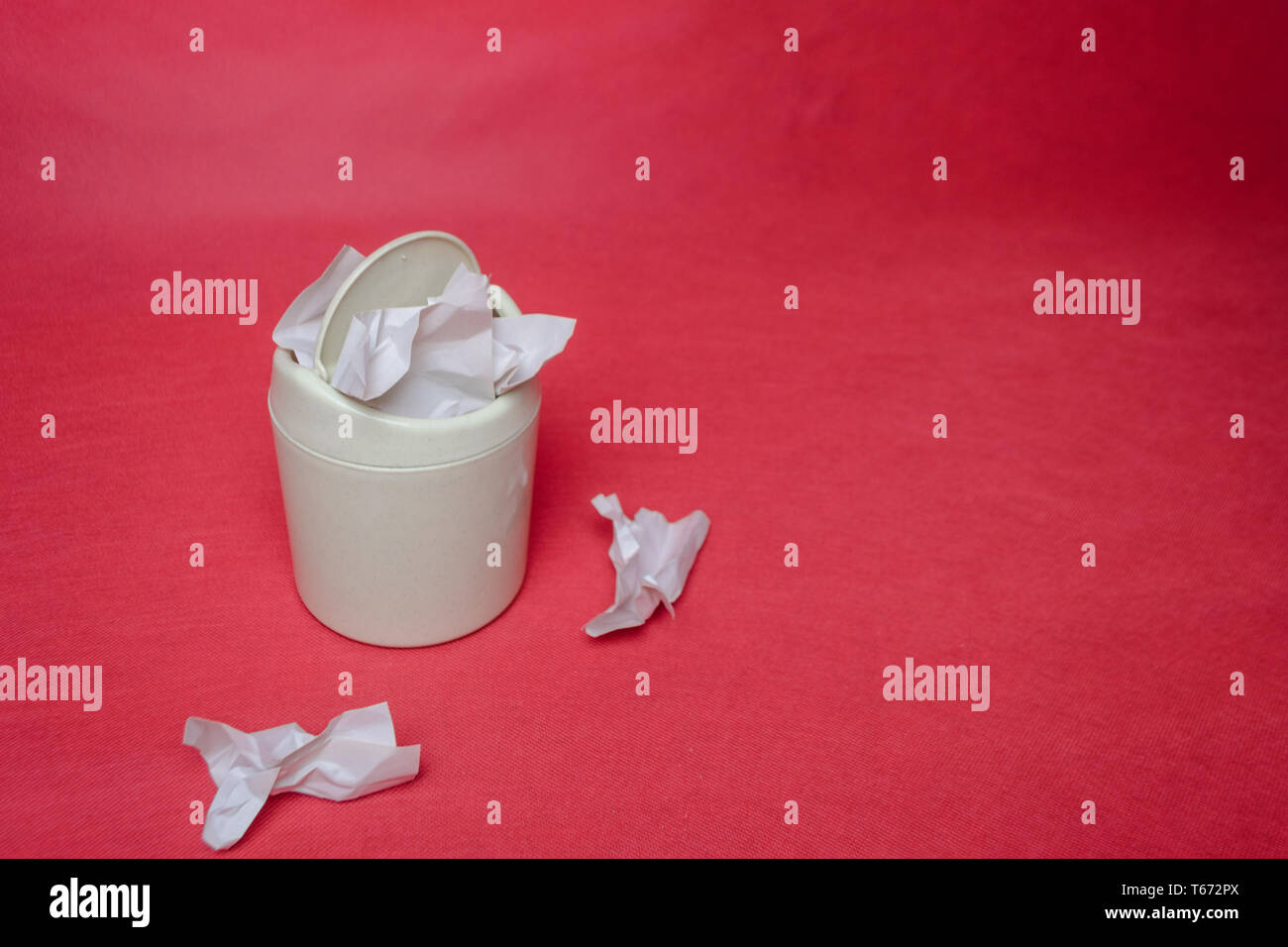 Light trash bin on a red background. Closeup of crumpled sheets of