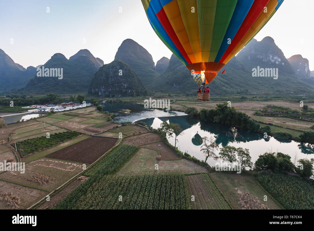 View of hot air balloon basket approaching landing spot in middle of rice fields and high mountains and a river Stock Photo