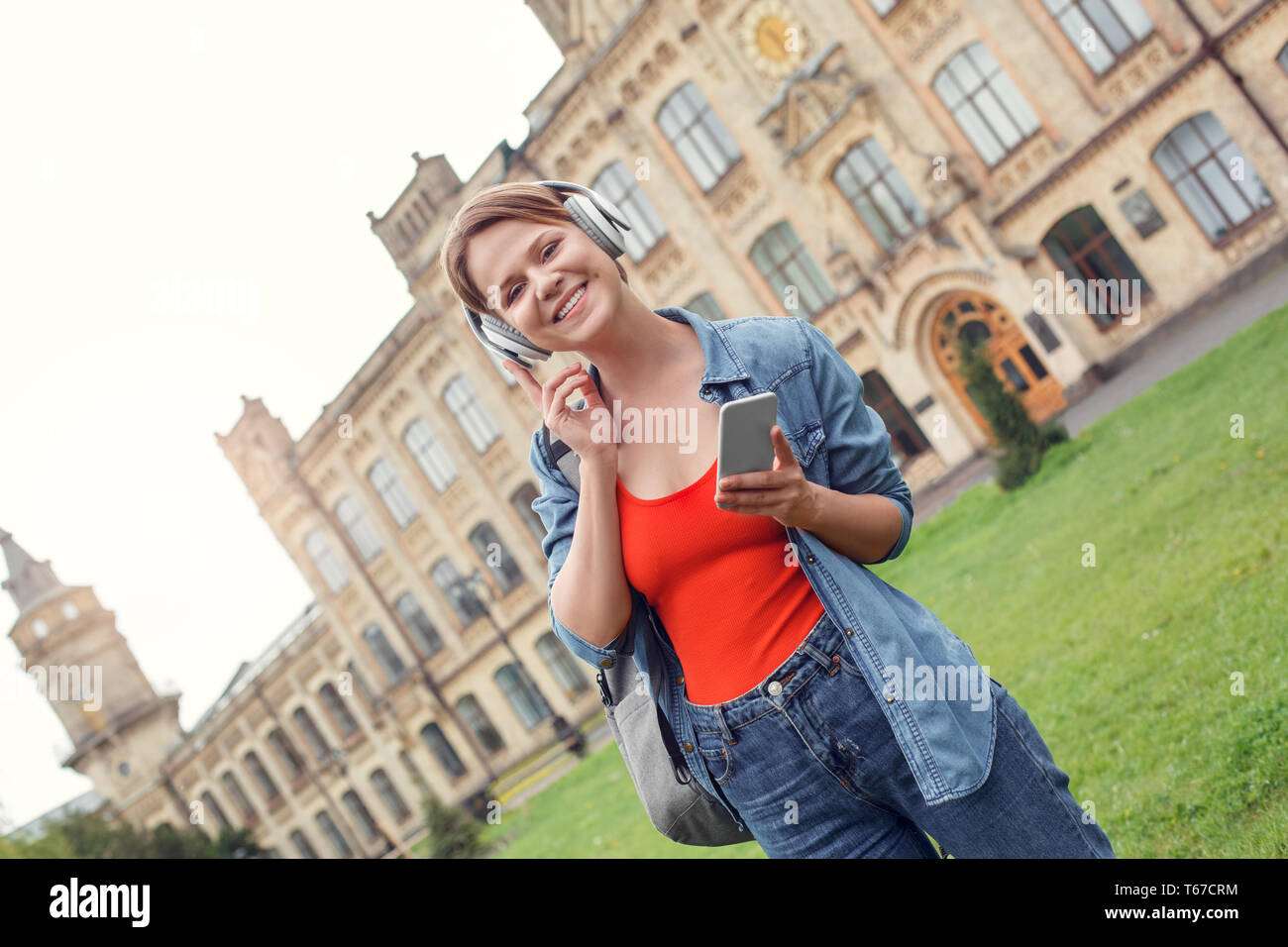 Young female student wearing headphones carrying backpack at university ...
