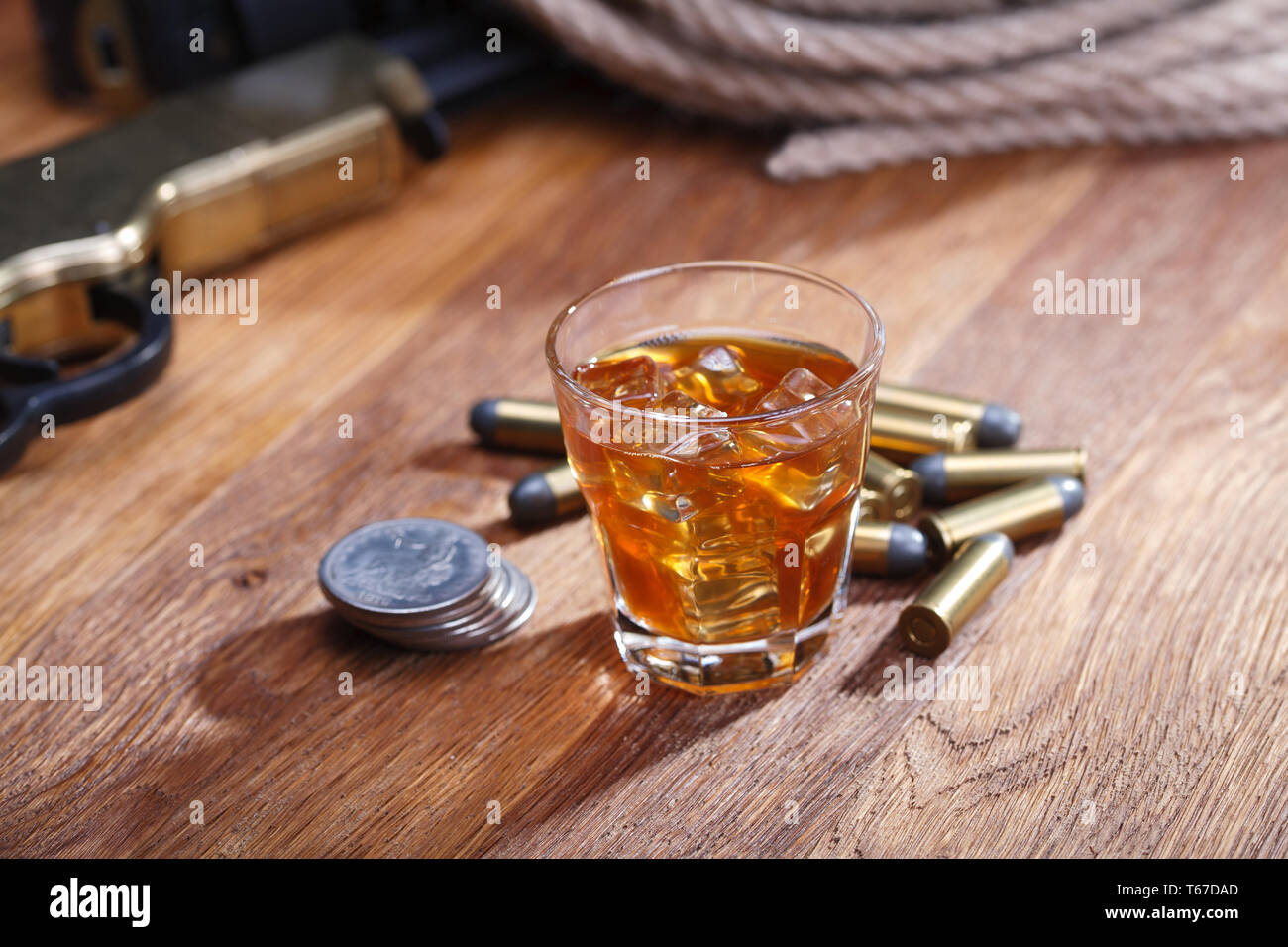 Wild west rifle and ammunitions with glass of whisky and ice with old silver dollar on wooden bar table Stock Photo