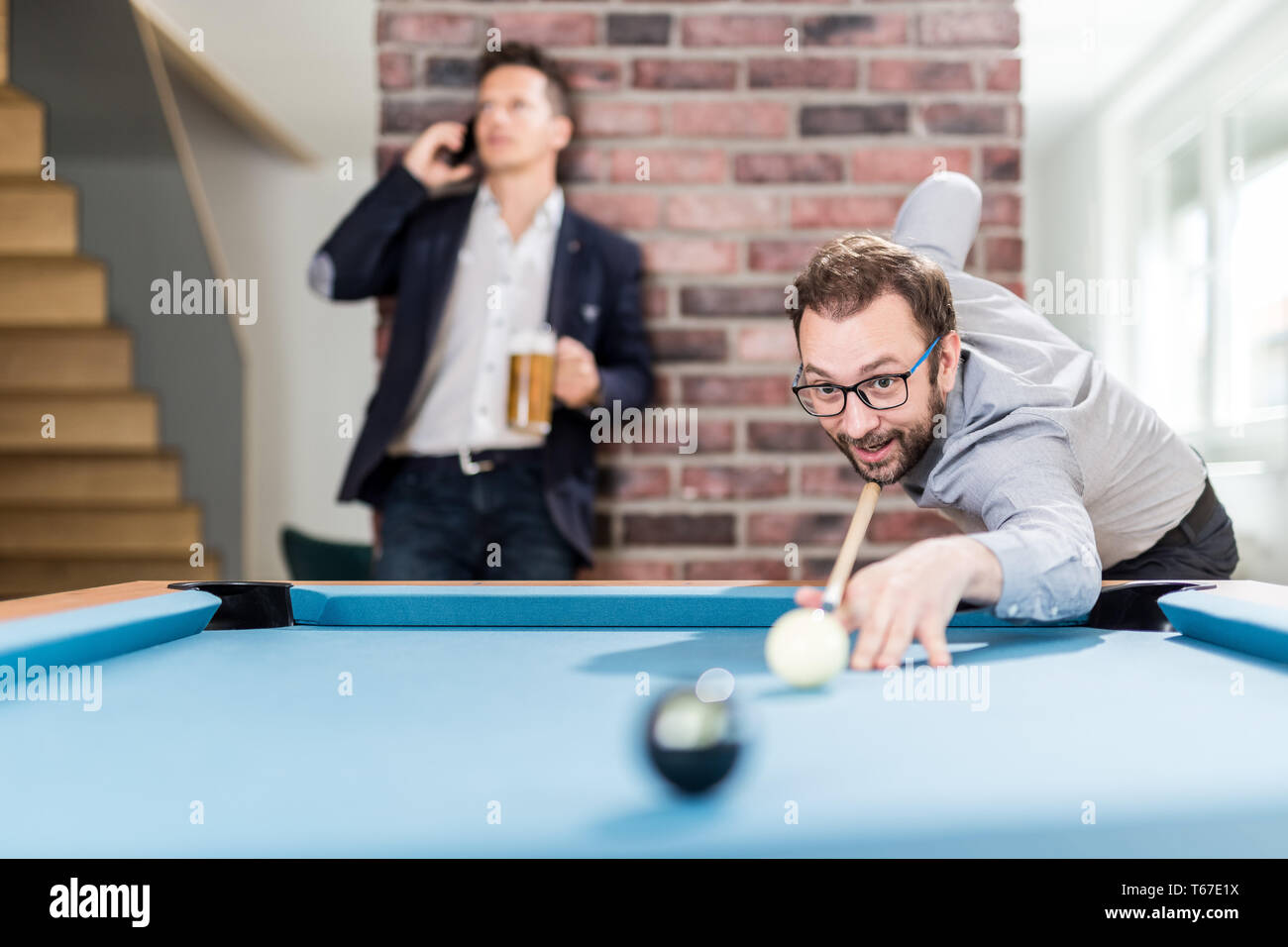 Business guys playing pool table billiard game in office chill room