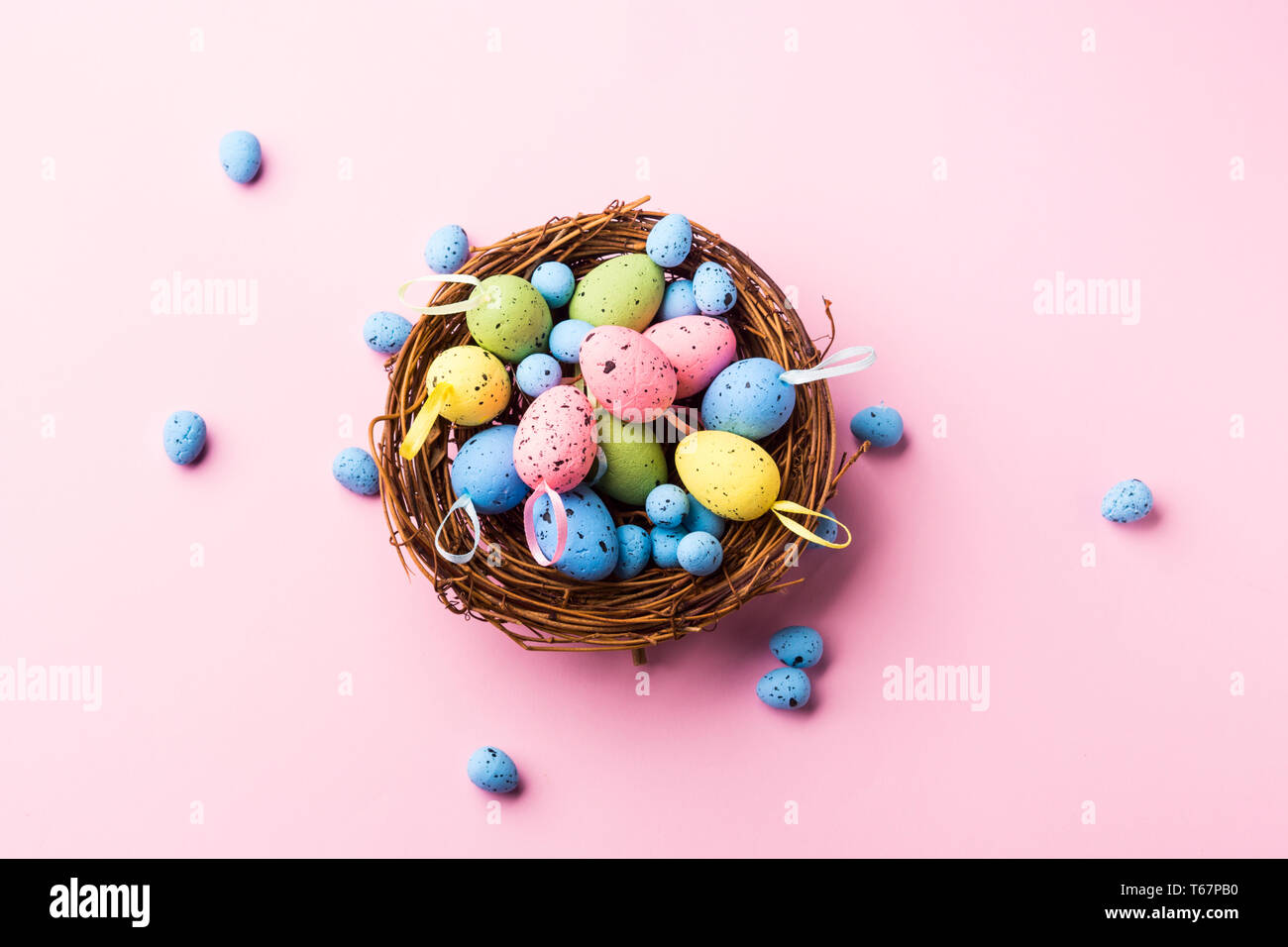 Colorful decor easter eggs in a nest on pastel pink background. Flat ...