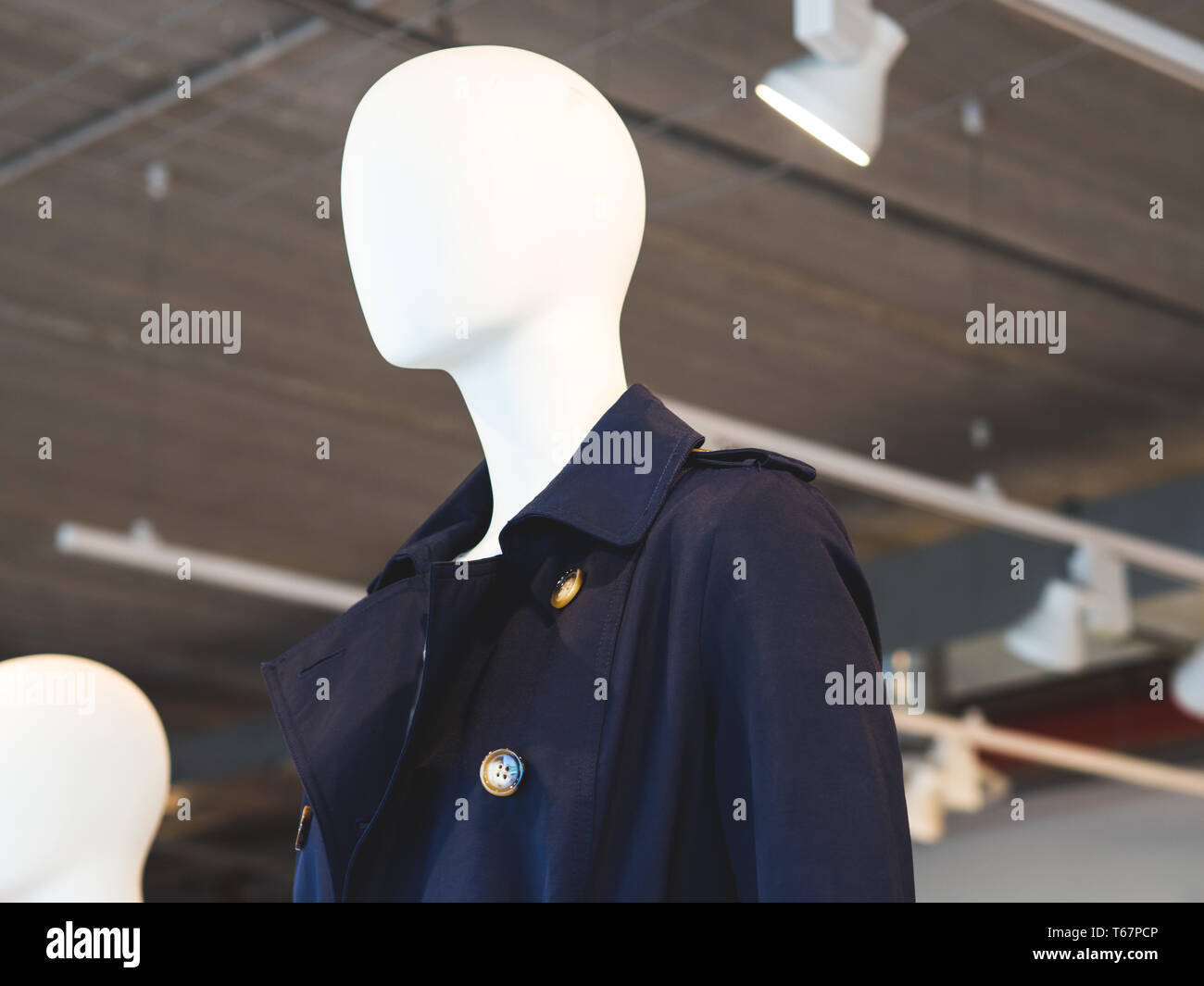 White mannequin wearing blue trench in a fast fashion store Stock Photo