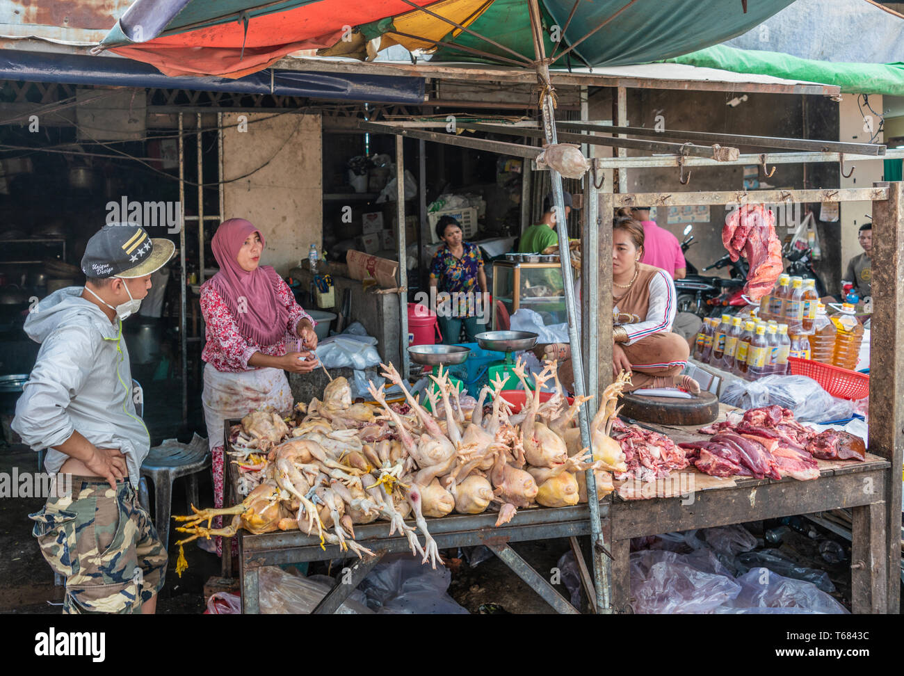Sihanoukville, Cambodia - March 15, 2019: Phsar Leu Market. Pink Hijab wearing Female butcher sells off pile of dead chickens in booth. Other merchant Stock Photo