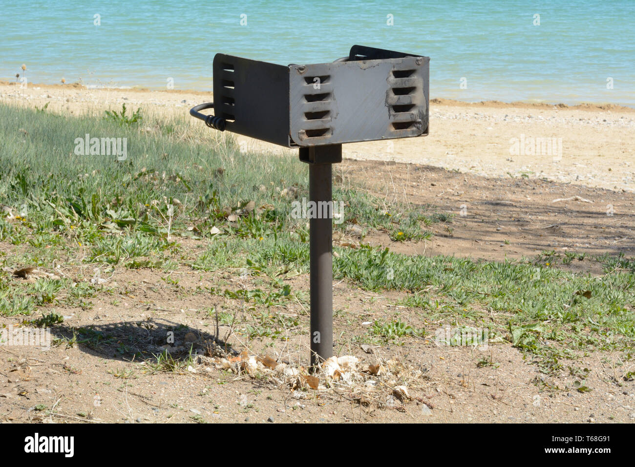 Empty outdoor park grill beside beach shore and lake in spring with new green plant growth Stock Photo